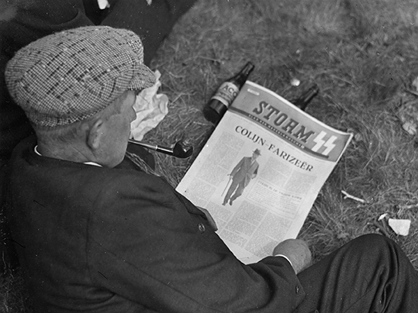 Een man leest een artikel over oud-premier Hendrikus Colijn in Storm, het weekblad van de Nederlandse SS, tijdens de boerenlanddag tegen het Bolsjewise tijdens de Tweede Wereldoorlog op 5 juli 1941 te Rolde. 