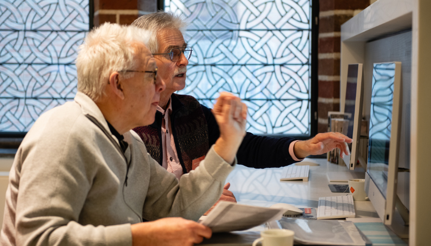 Studiezaal Drents Achief. Medewerker helpt bezoeker achter PC