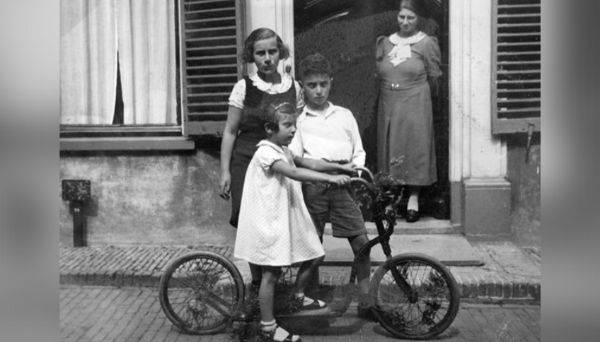 Drie kinderen met step op de stoep. Vrouw kijkt toe.